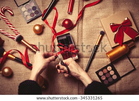 Female hands are wrapping cosmetics in christmas gifts on jute background