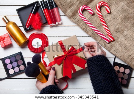 Female hands are wrapping cosmetics in christmas gifts on white wooden background