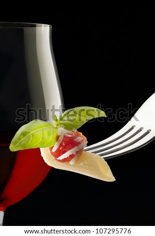 red wine glass and fork with macaroni on black background