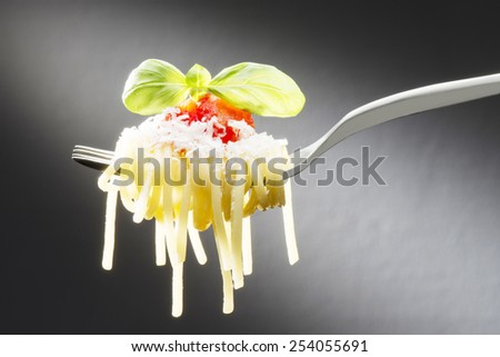 fork with spaghetti tomato sauce and basil on dark background
