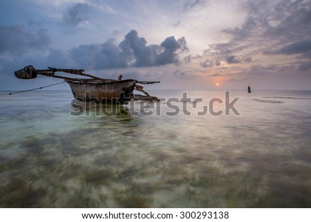 A Dhow fishing boat during the Zanzibar sunrise in the Indian ocean, and a lone fisherman.
