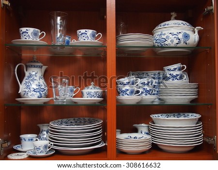 Mugs, cups and plates with blue and white pattern of flowers and onions. All neatly cleaned up in a wooden kitchen cabinet.