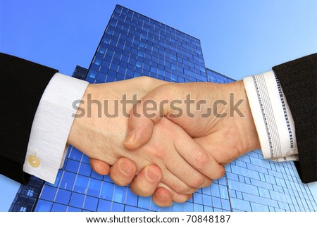 Businessmen shaking hands in front of the Skyscraper on the blue Sky
