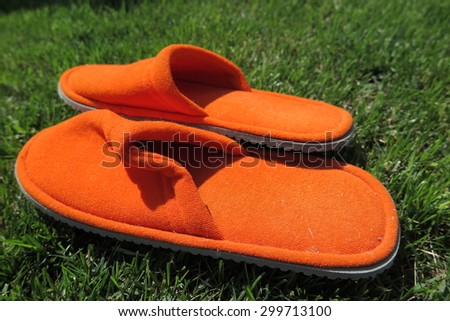 Orange house slippers on mown lawn grass in the summer garden
