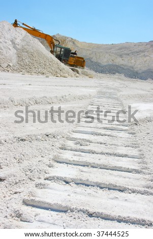 Caterpillar excavator and a track in chalk pit against a blue sky