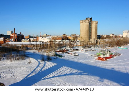 A view from the bridge at a frozen river and an industrial city against a blue sky