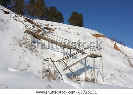 Stairs with landing against a snow slope against pines and a blue sky