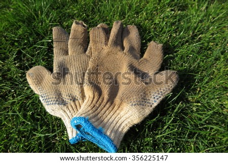 Dirty and worn-out gardening textile gloves on the mown lawn after hard work in the autumn garden