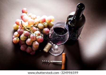 glass and green bottle of red wine with bunch of pink grapes,cork and bottle opener