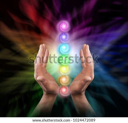 Sending Chakra Healing Energy - Male parallel hands facing upwards against a multicoloured background of energy and the Seven Chakras floating between his hands