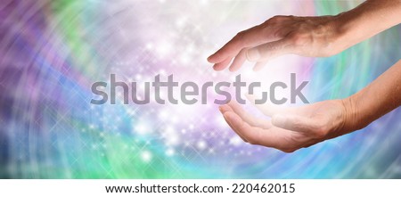 Close up of healing hands cupped with beautiful magical sparkling swirling colored energy on wide background