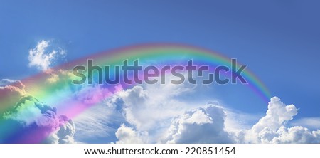Wide blue sky with fluffy cloud formations clouds and a rainbow arcing off into the distance