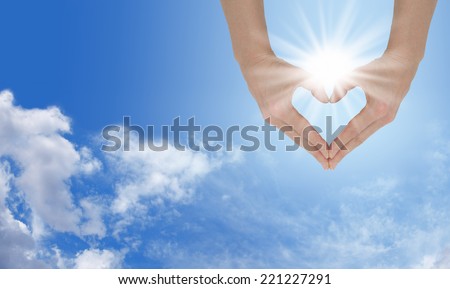 Loving the Sunshine - Female hands forming a heart shape capturing the sunburst behind on a wide blue sky and fluffy cloud background