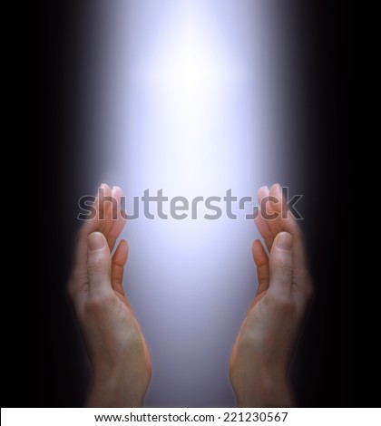 Woman\'s hands outstretched with shaft of white light and cross between on a black background