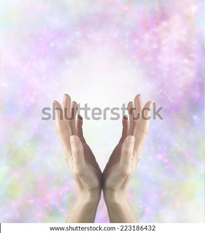 Gentle healing energy - Female healing hands cupped and reaching upwards with white light between palms and a beautiful delicate pink and pastel colored background