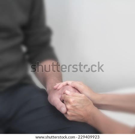 Cropped image focusing on therapist holding client\'s hand offering comfort with a soft blur effect on everything except the hands.