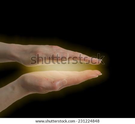 Female energy healer\'s hands held parallel with a golden light between on a black background