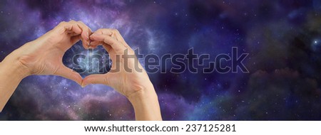 Heart hands loving the Universe - Female hands making a heart shape on a wide deep space background showing a nebula behind the heart shape