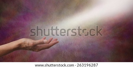 Ask Believe Receive - Female hand outstretched with a shaft of white light streaming across from the top right hand corner as if receiving energy on a wide dark colored rustic stone effect background
