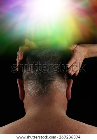 Healer working on Crown Aura Energy - Back of a man's head with female hands hovering either side on a black background with an ethereal colorful burst of light above in the crown chakra area