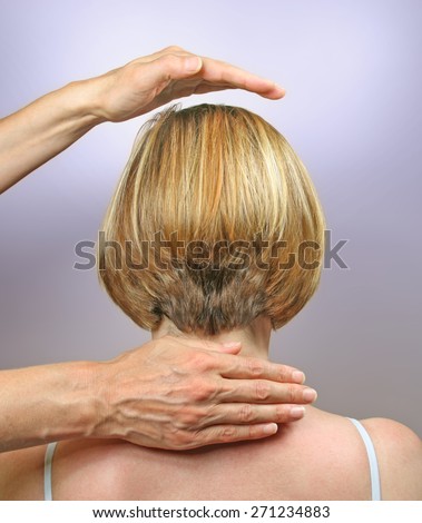 Demonstrating hand positions for channeling healing - Female healer\'s hands hovering in crown area and back of neck of female client, channeling energy, with a soft lilac energy around crown area