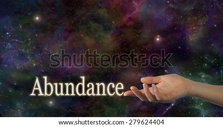 Universal Abundance - Female hand facing up with the word Abundance touching the index finger on a deep space night sky background providing plenty of copy space above