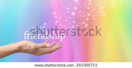 Friendship in the Palm of your Hand - Female hand outstretched and facing upwards with the word \'friendship\' floating above on a rainbow colored background with sparkles flowing from the word