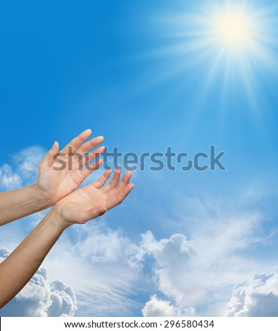 Female hands reaching up towards a bright sun burst on a blue sky background with fluffy clouds and plenty of copy space