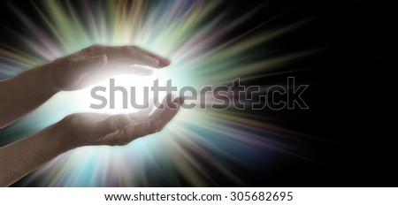Miracle maker - pair of parallel female healer\'s hands with a bright white and rainbow colored light energy formation between on a wide black background with plenty of copy space