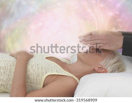 Channeling Healing Energy - Female patient lying with eyes closed and male healer with hands hovering channeling energy with misty sparkling pink energy field all around