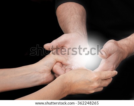 Sharing an Energy Experience - female healing mentor holding male students open hands with a bright light energy orb between on a black background and copy space