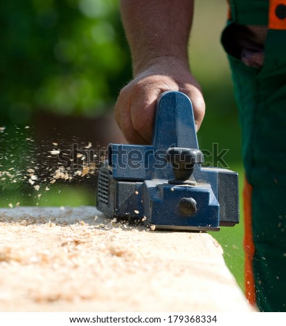 Carpenter with electric wood planer at work outdoor.