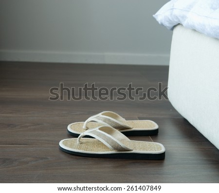 Bamboo flip flops on the ground near bed.
