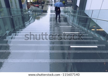 wet city stairs with moving man under blue umbrella; focus on foreground stairs