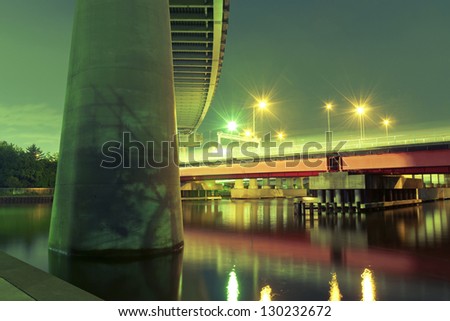 huge highway support on foreground with red bridge illuminated by night in Tokyo, Japan