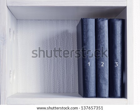 three similar black books with printed numbers on white bookshelf