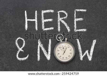 here and now phrase handwritten on chalkboard with vintage precise stopwatch used instead of O