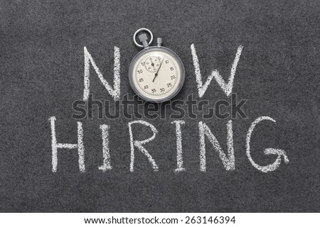 now hiring phrase handwritten on chalkboard with vintage precise stopwatch used instead of O