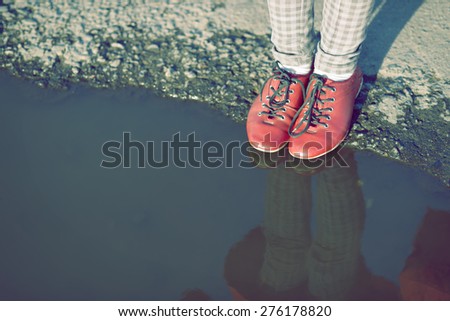 child legs in red shoes close to the edge of big puddle