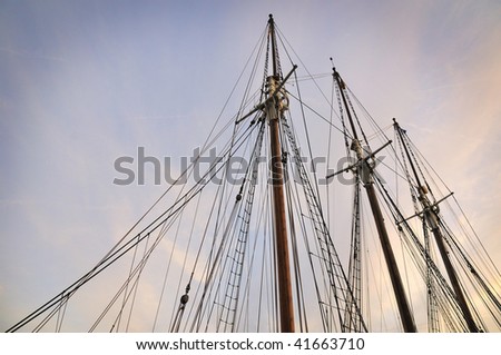 three wooden ship masts with ropes over scenic evening sky