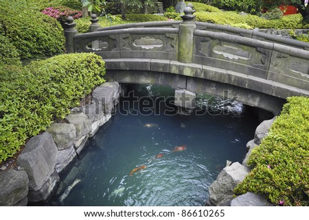 scenic stone bridge over blue water with red fishes in Japanese stone garden