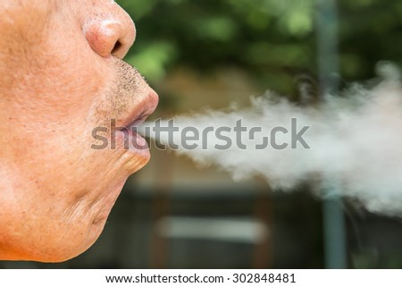 Thick cigarette smoke comes out of the mouth of the smoker old man.