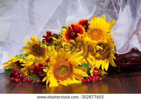 bouquet of sunflowers, viburnum and red daisies on a background of a basket and a white transparent fabric on a wooden table