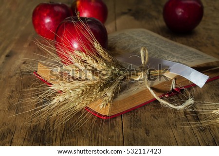 red apples and ears of wheat on the book on a wooden table on a blurred background