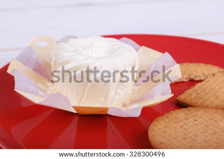 cream cheese in an environmentally friendly packaging made of wood with a round pastry on the red plate, top view, side view,