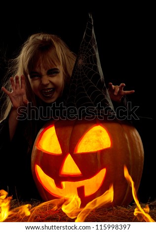 Portrait of little girl in black hat and black clothing with pumpkin on black background