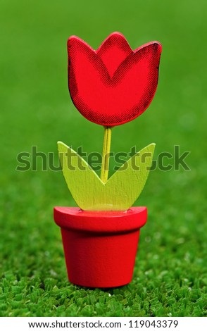 Nice artificial flower in small flowerpot on artificial green grass