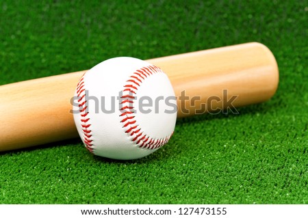 Close-up of wooden bat and baseball ball on artificial green grass