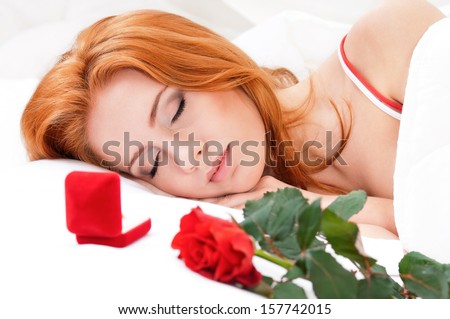 Beautiful girl is sleeping on white bed. Flower and wedding ring in a gift box on a pillow next to her