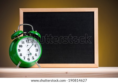 Big green alarm clock with blackboard on dark yellow background